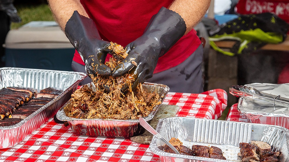 BBQ Battle contestant wearing gloves and shredding cooked meat in a pan