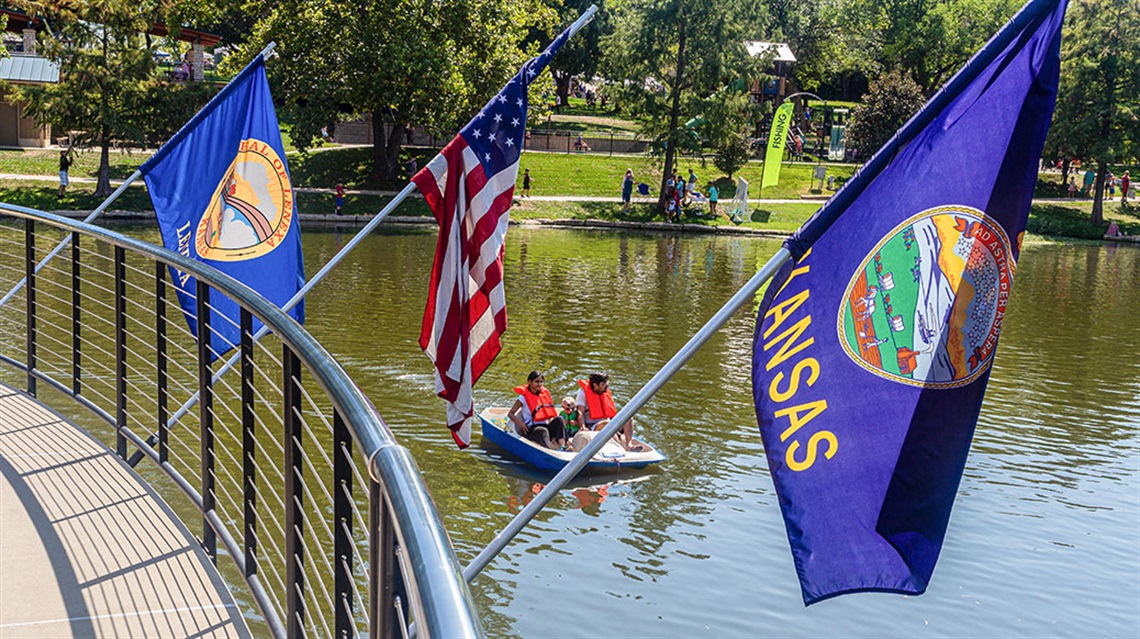 flags along walkway overlooking people paddle boating in pond