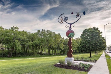 Large whimsical scuplture. Amusing Breeze: This piece features a colorful, abstract bicycle atop a mosaic glass ball by artist Chris Duh. It is located along 87th Street Parkway at Sar-Ko-Par Trails Park.
