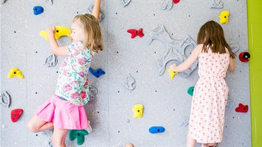 Two girls climb rock wall