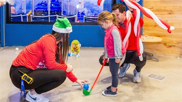Adults help girl set up mini golf shot