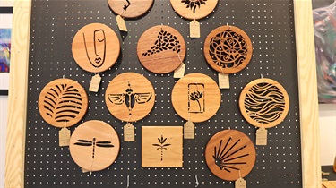 Handmade round wood trivets with patterns hanging on a pegboard