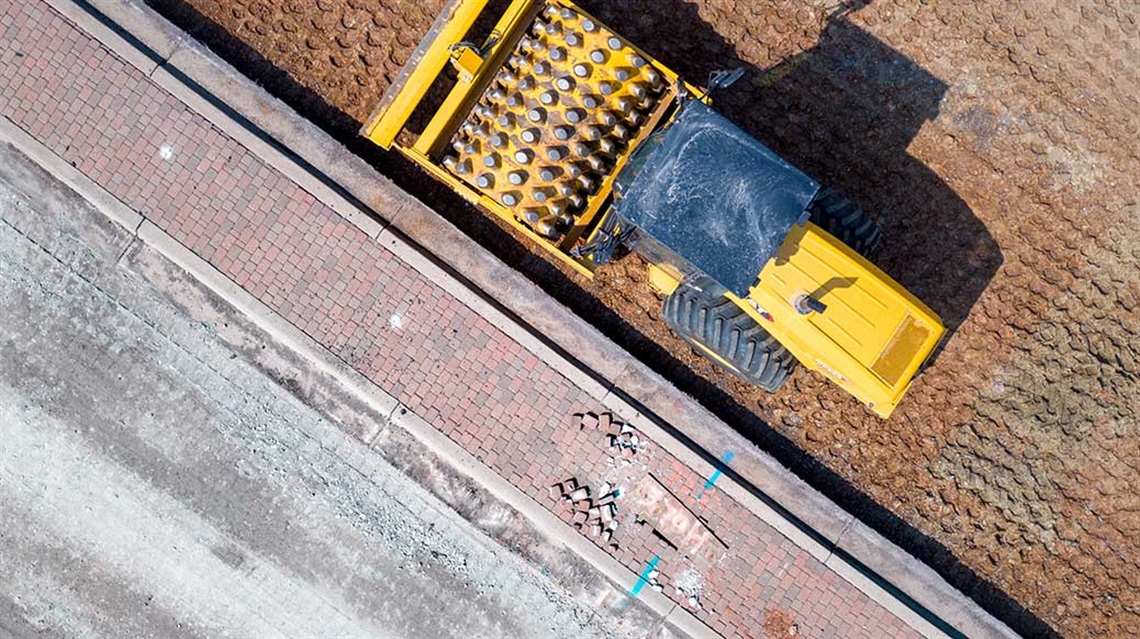 Aerial view of tamping roller equipment next to excavated road subbase and brick pavers