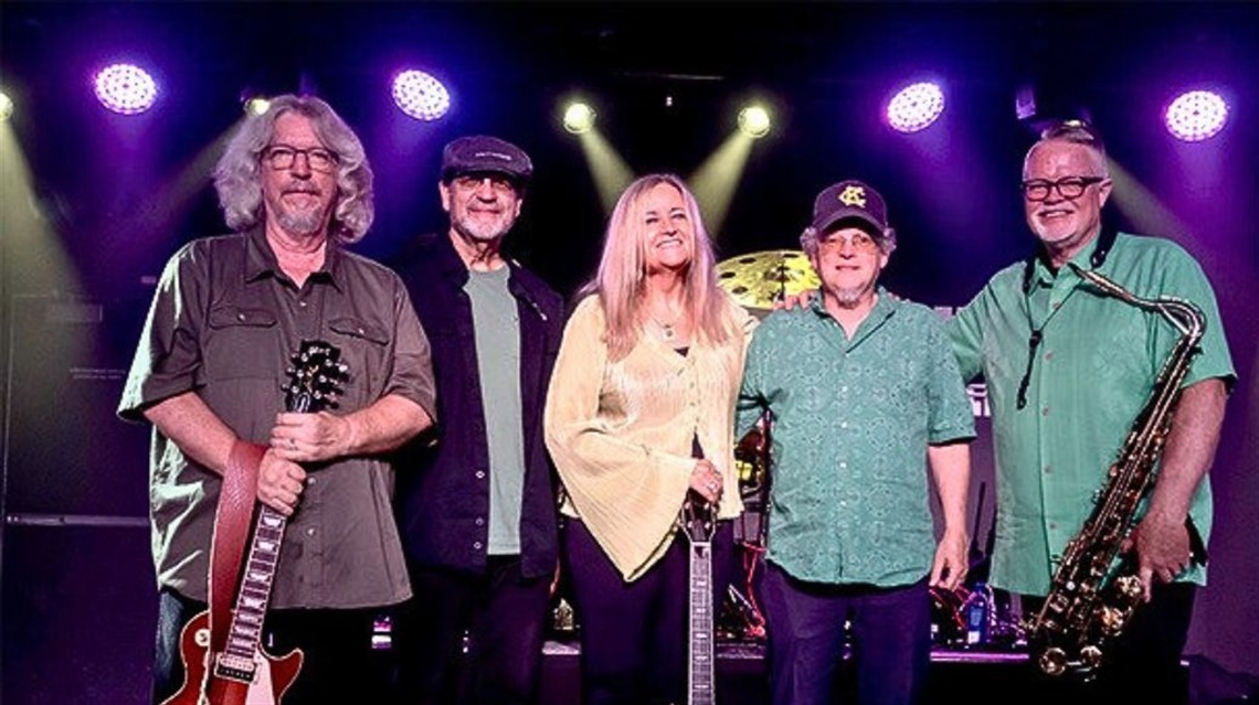Five-member band smiles with instruments on stage