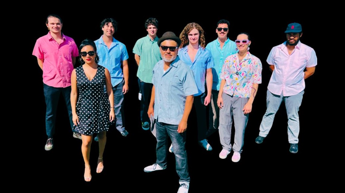 Nine members of the KC Latin Jazz Orchestra stand against black backdrop