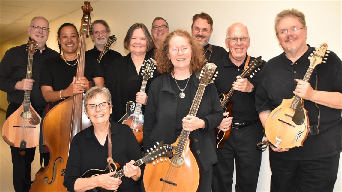 Ten orchestra musicians hold various instruments and smile