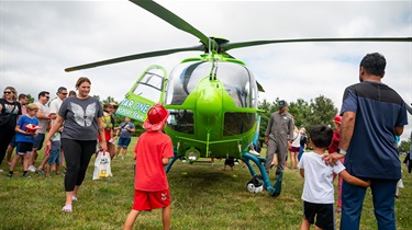 Crowd milling around helicopter in a field