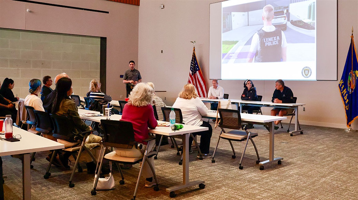 Police officer presents PowerPoint to room full of people seated at tables