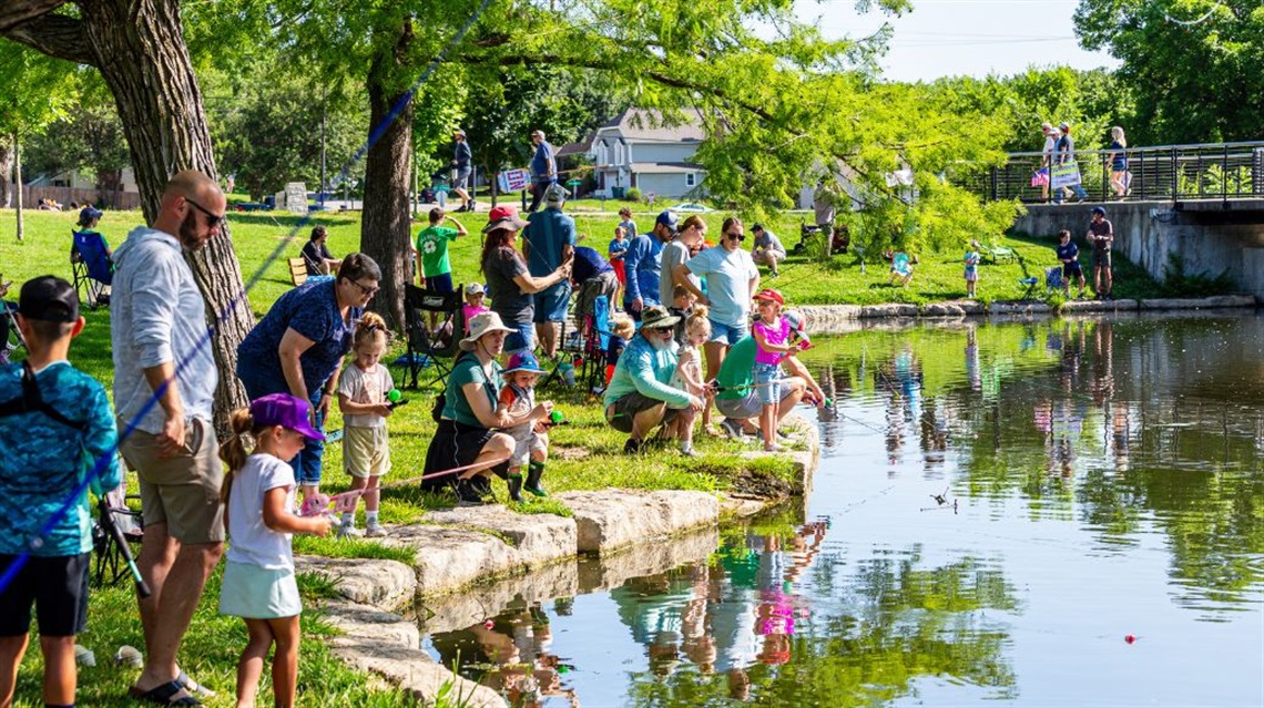 People standing or sitting while fishing at the edge of Rose's Pond at Sar-Ko-Par Trails Park.