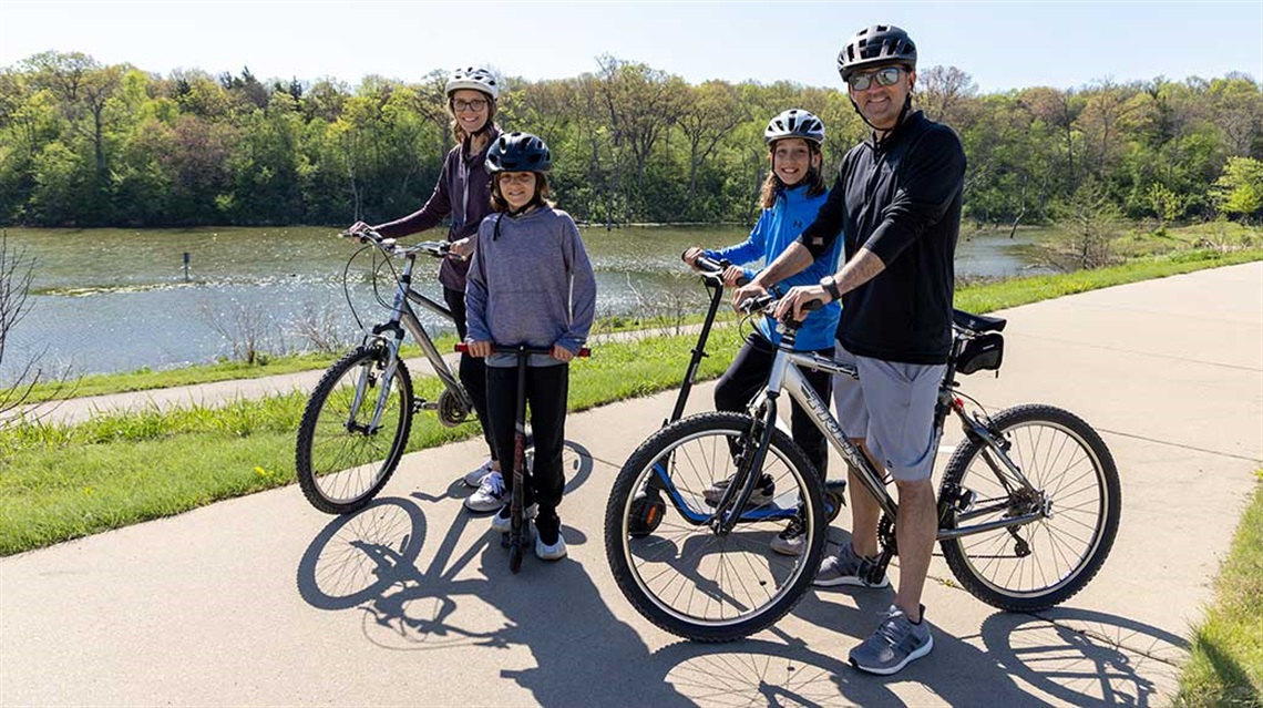 Two adults in helmets standing near bikes and two kids in helmets standing near e-scooters