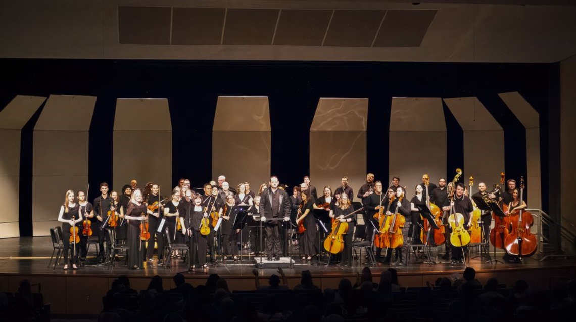 Members of community orchestra and conductor stand for applause