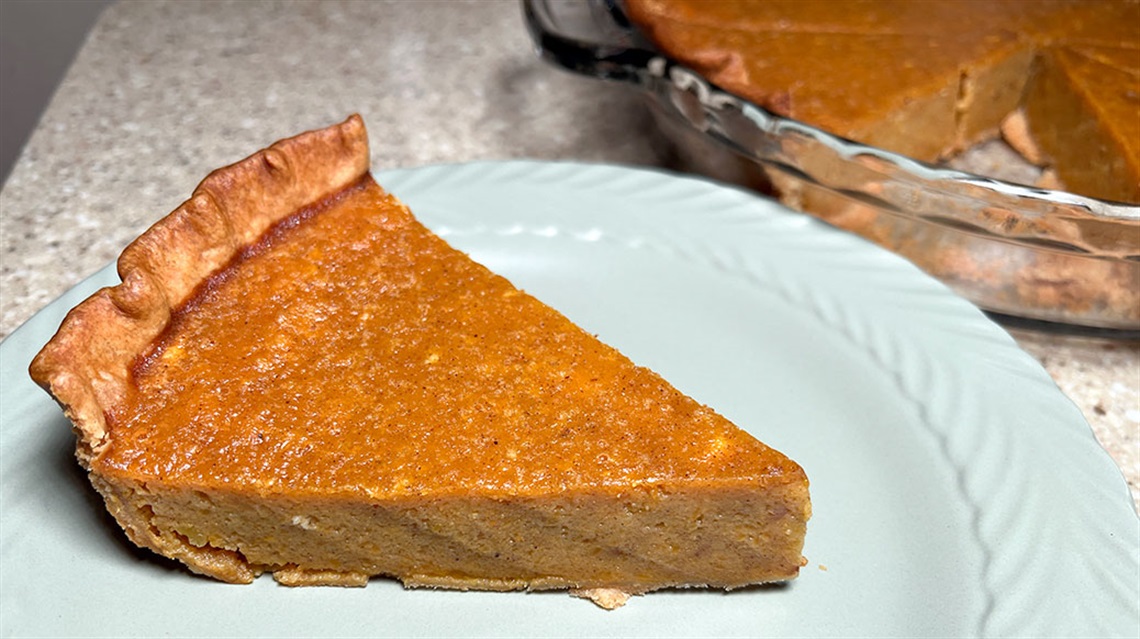 slice of butternut squash pie on plate next to pan full of pie