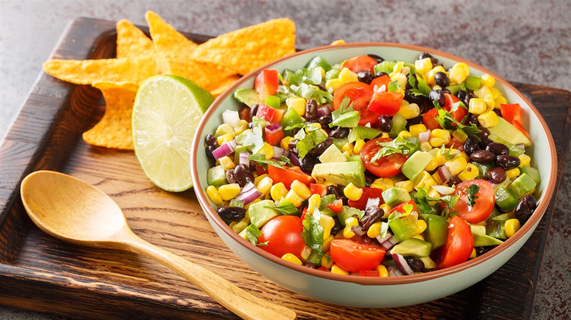 Bowl of cowboy caviar dip with wooden spoon, tortilla chips, lime