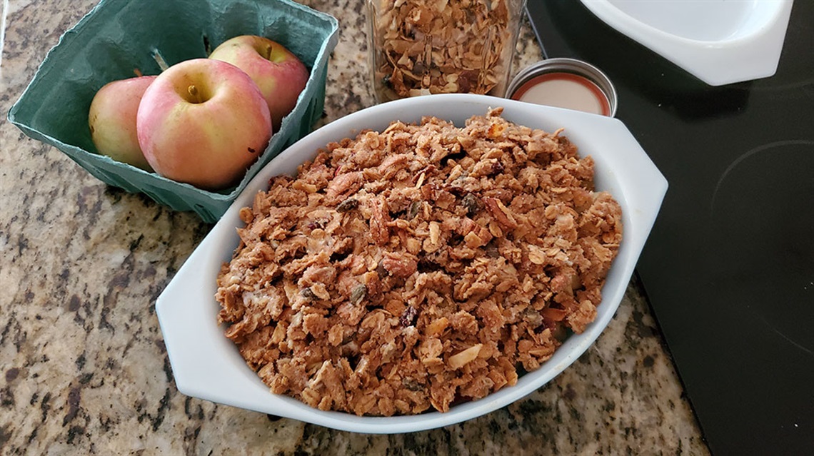 Birds-eye view of dish of granola on counter with apples nearby