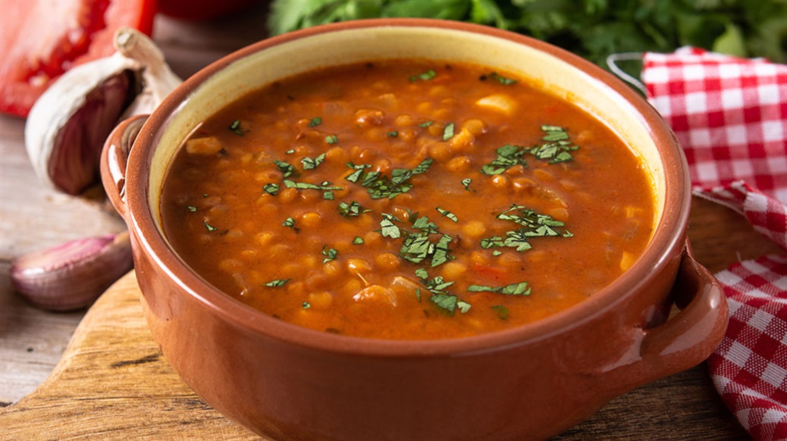 Closeup of bowl of lentil soup on cutting board with checkered napkin