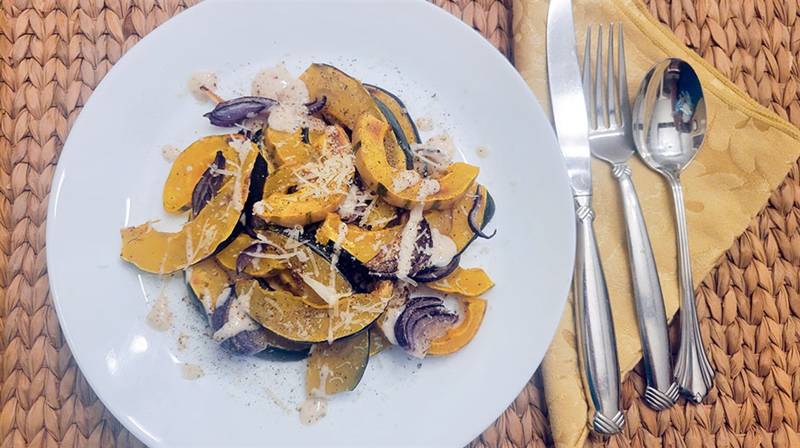 roasted squash salad on plate next to silverware and napkin