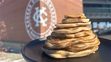 Stack of pancakes sitting on platter with KC logo in background on brick wall