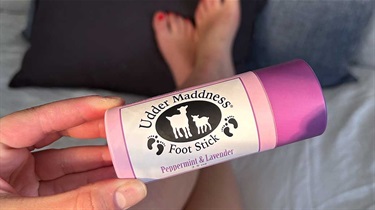 Hand holding peppermint and lavender lotion foot stick with crossed legs in background