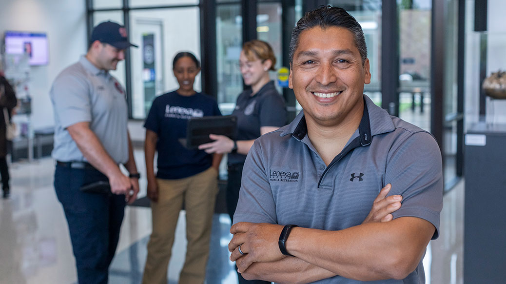 Employee smiling with arms crossed and other employees behind him