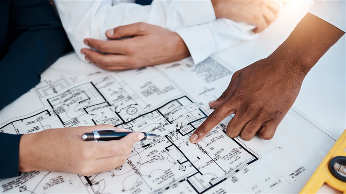 closeup view of people's hands pointing to areas of a building plan on a table