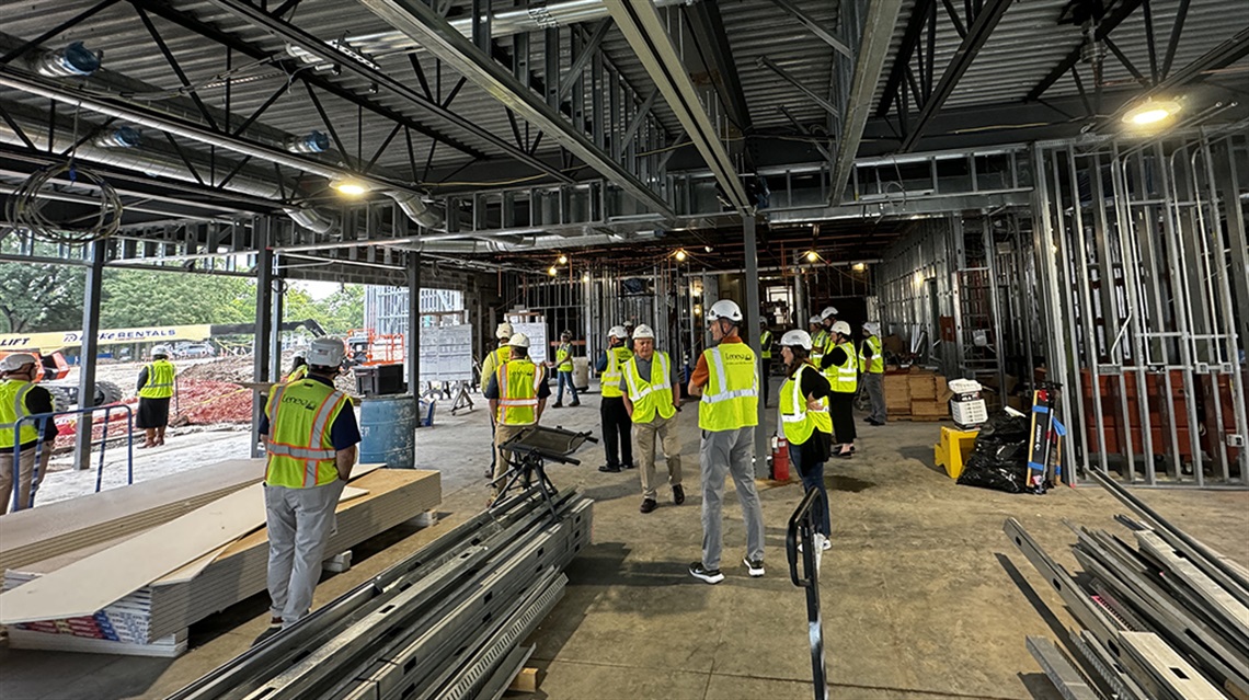 Group of staff and contractors in hard hats and yellow vests inspecting building renovation.