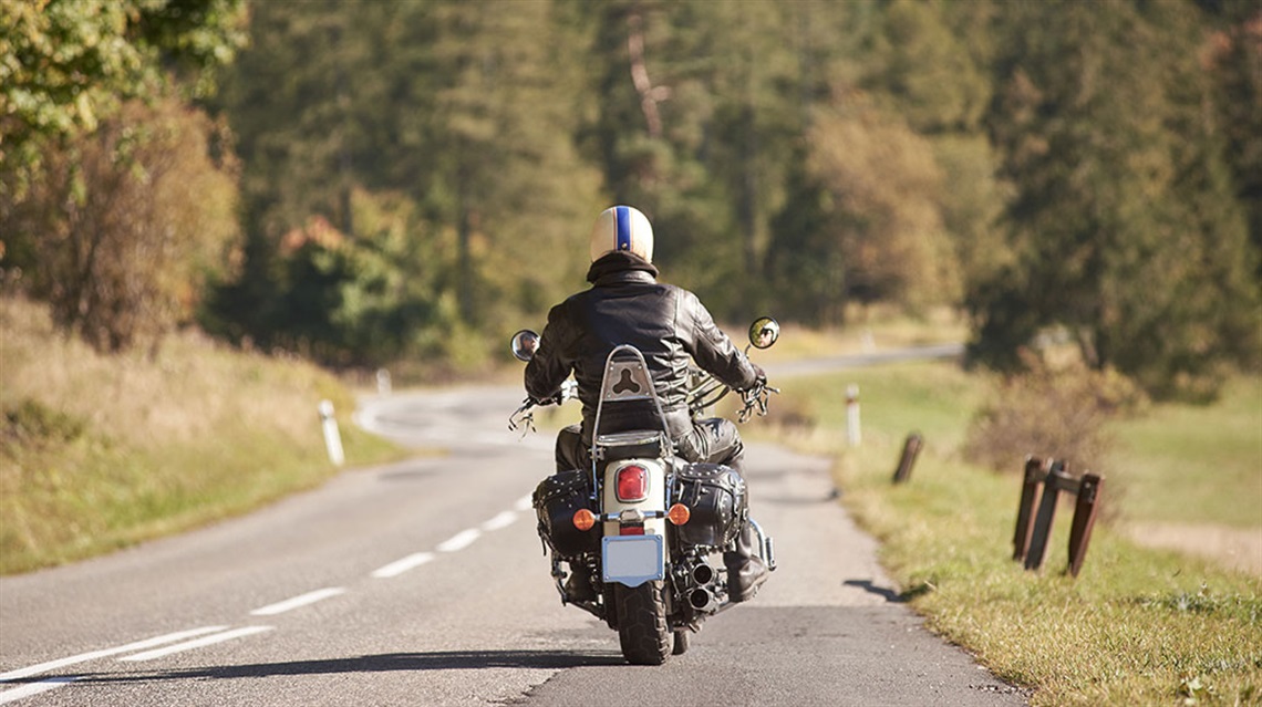 View of back of man on motorcycle riding away on road
