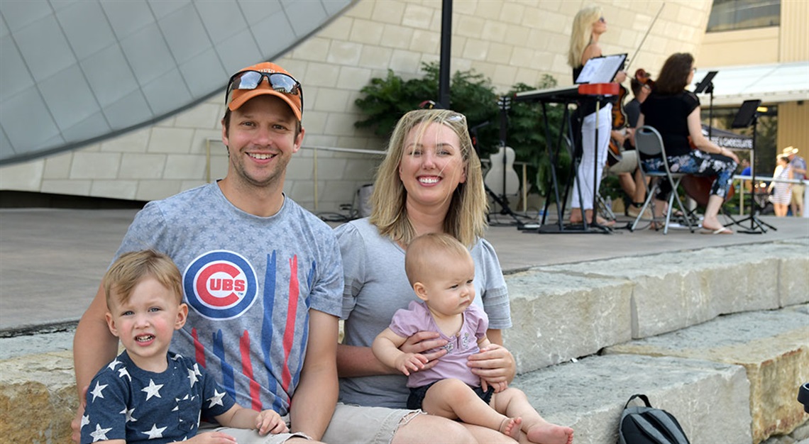 Family with young children seated on edge of stage with band playing in background