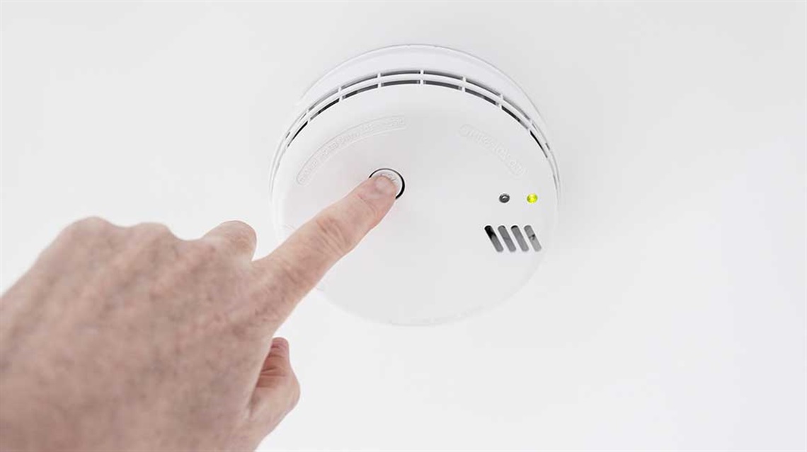 Closeup view of hand pressing button to test smoke alarm