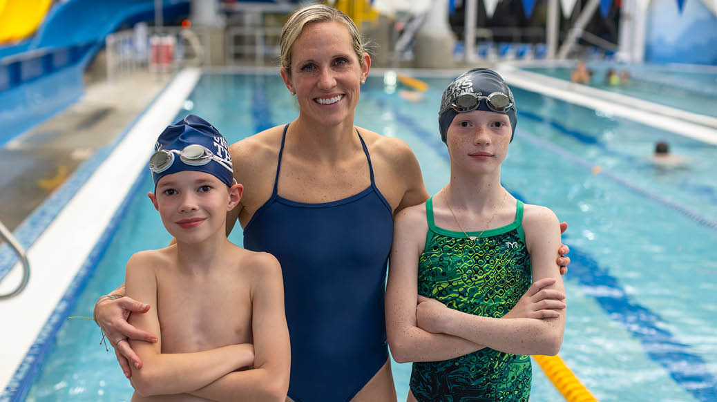 Beth with her twin kids smiling in front of the Lenexa Rec Center indoor pool