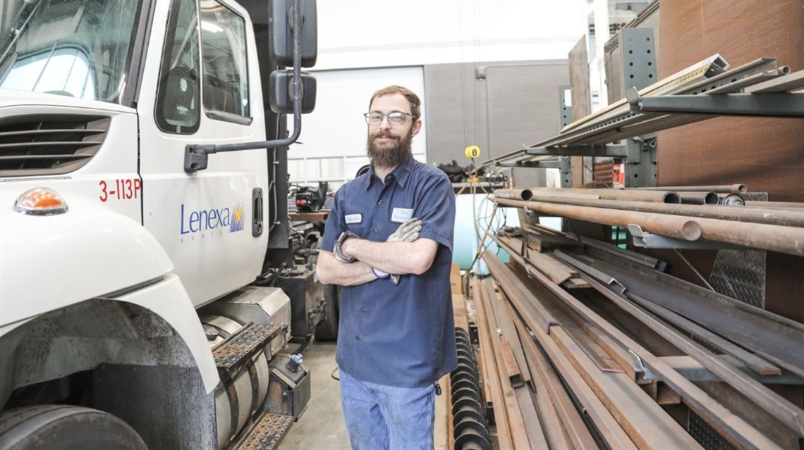 Austin Axmann smiling with his arms crossed with city vehicle in background