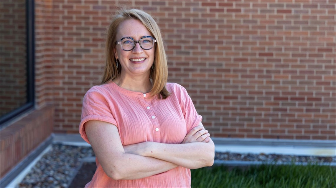 Smiling woman with crossed arms stands in front of brick wall