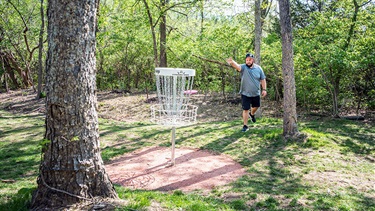 Man throwing disc at disc golf basket