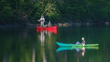 Man fishing in canoe near man floating in kayak