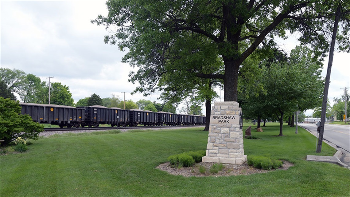 Bradshaw Park monument sign with green grass and train in background