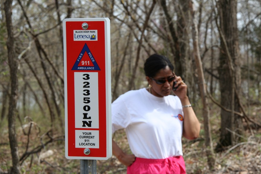 Woman talking on a phone next to a trail Emergency sign