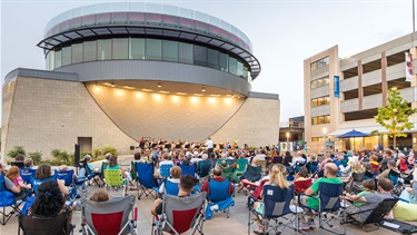 Seated crowd watches orchestra perform on outdoor stage
