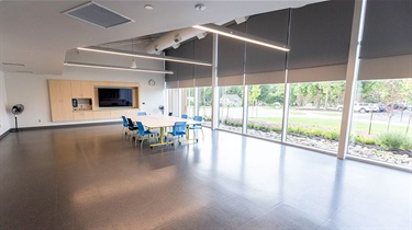View of room looking southeast with cabinet wall, tables with chairs and wall of windows