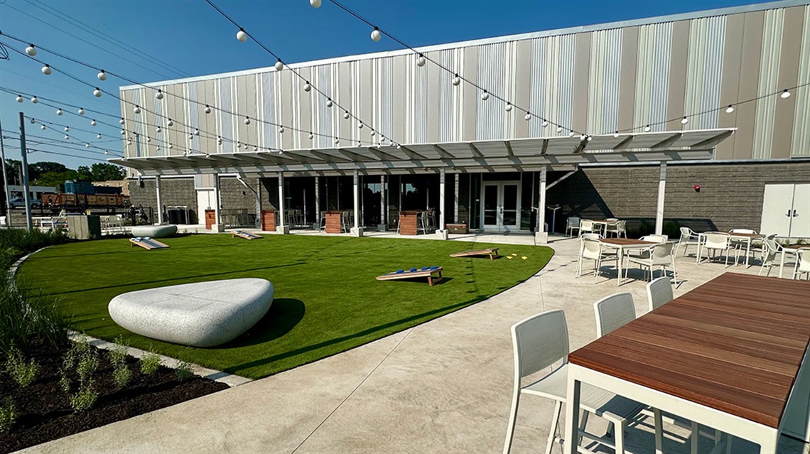 Covered and uncovered seating surrounding turf area with cornhole boards