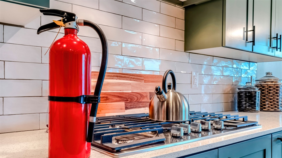 A fire extinguisher sits atop a kitchen counter next to a stove