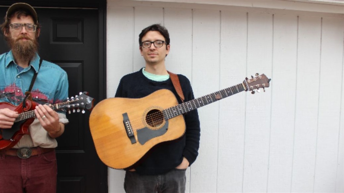 Two men wearing glasses and holding guitars