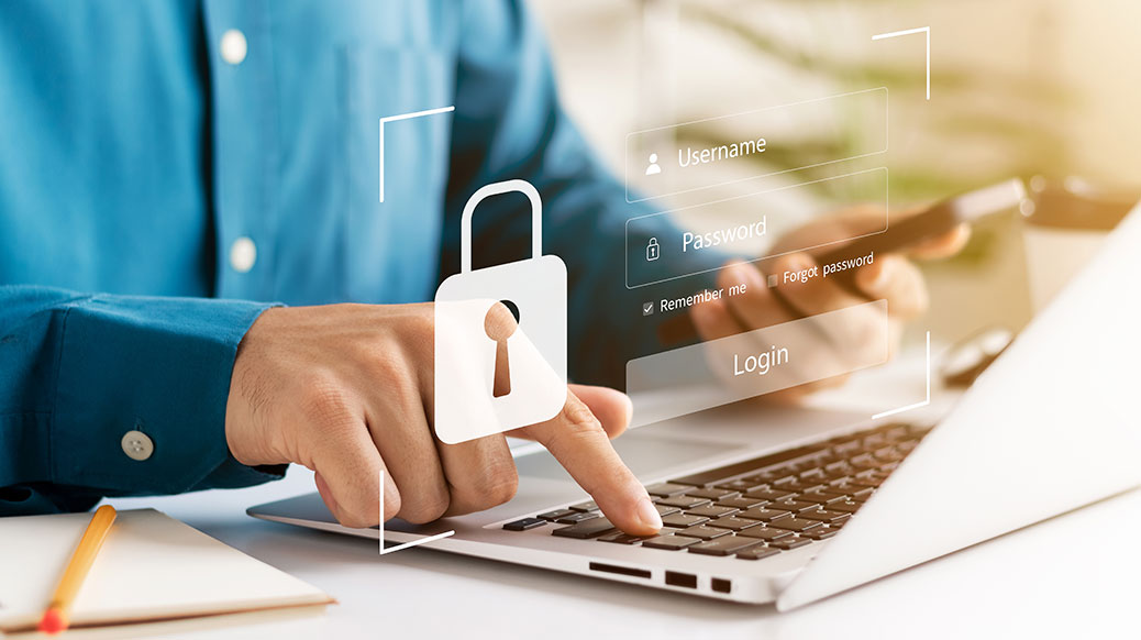 adult male typing on laptop with cell phone in hand