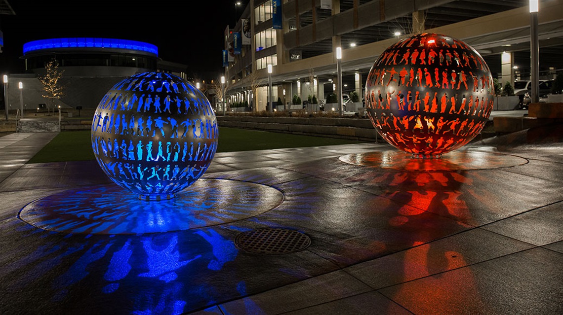 Two stainless steel orbs with many human shape cutouts lit up in blue and orange at nighttime