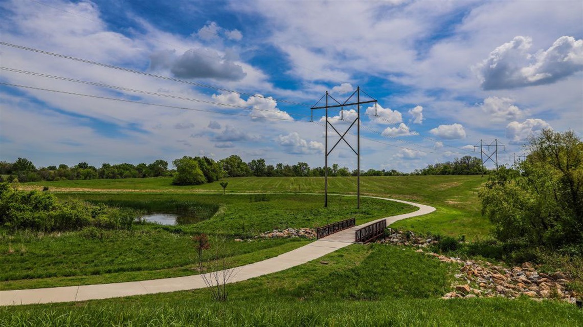 Distant view of trail with bridge winding through a park with power lines in background