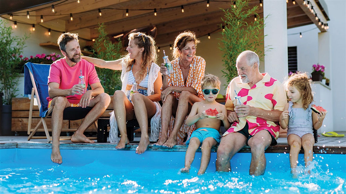 Group of adults and children sitting on edge of a pool
