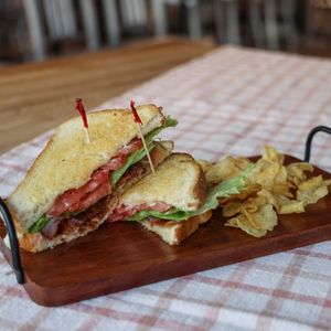 Classic BLT with chips on wooden slab on top of table