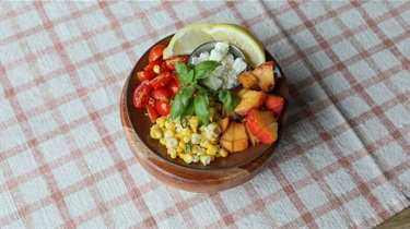 Fresh ingredients for salad including sliced lemons, peaches, corn, tomatows and feta cheese